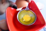 Cracked egg in scoop spoon in bowl