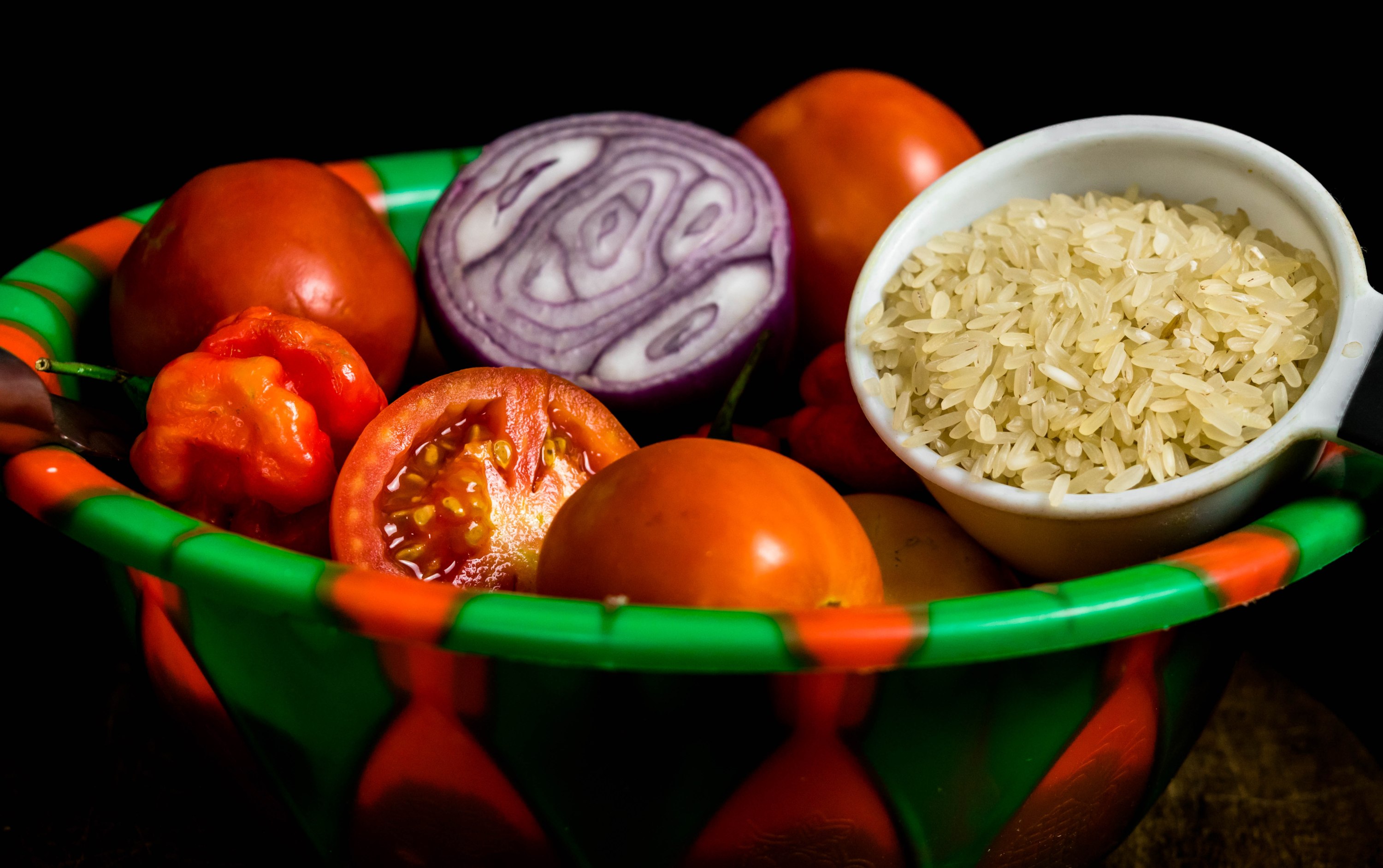 Rice, Sliced tomato and sliced onion, Scottish bonnet peppers in green and red plastic bowl for Nigerian stew concept isolated on black background